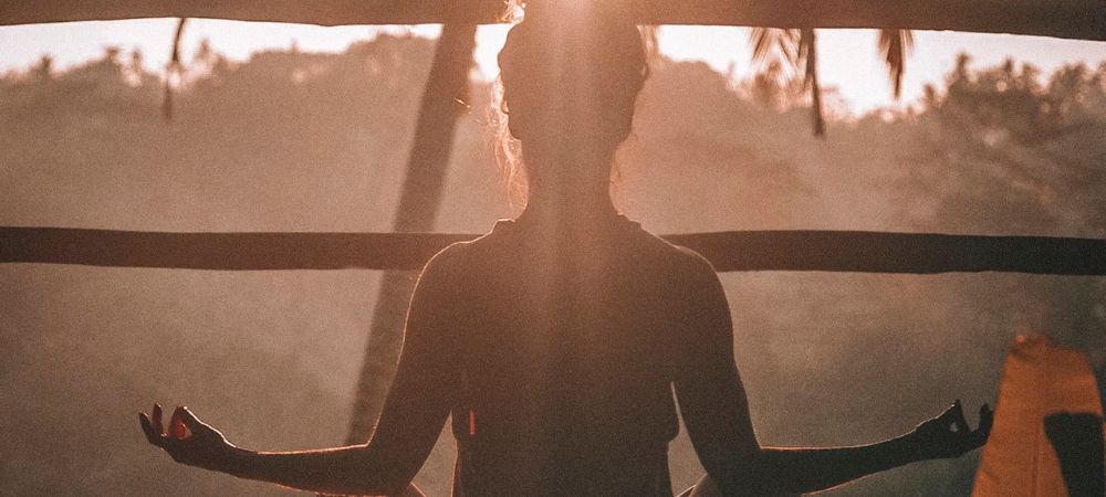 Woman doing meditation in front of the sun.